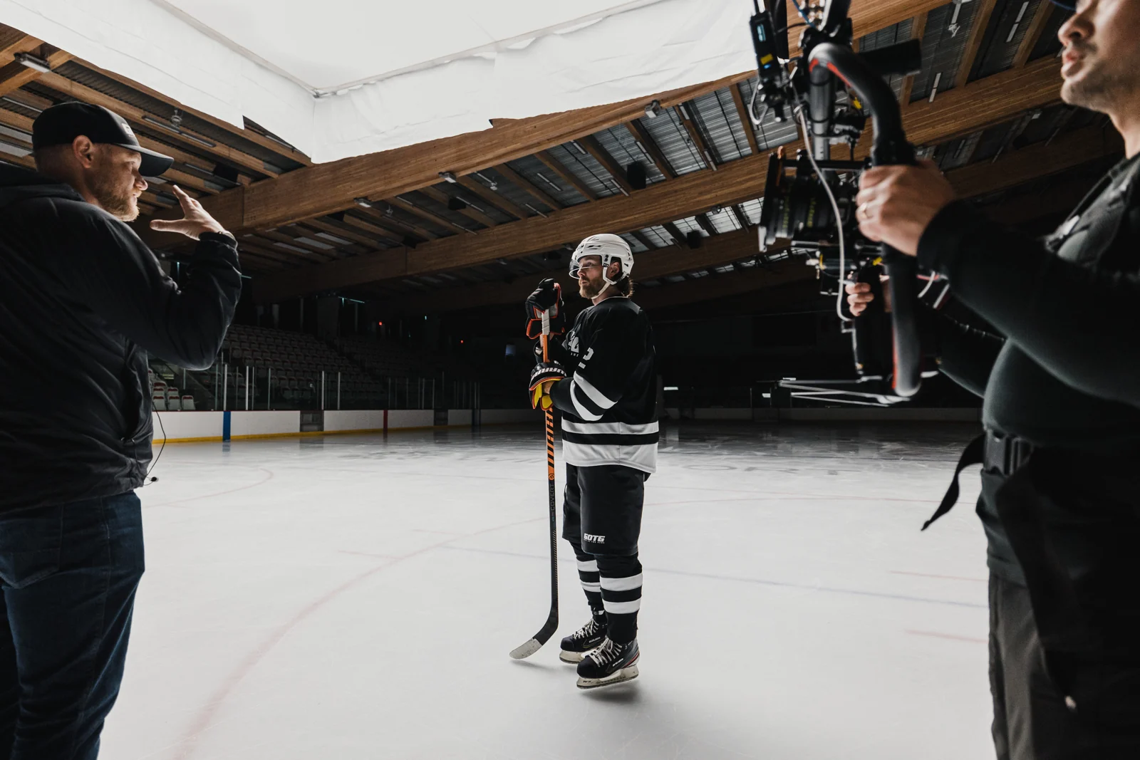 Direction on the ice beneath a large overhead diffusion frame, with a cinema camera beside the athlete